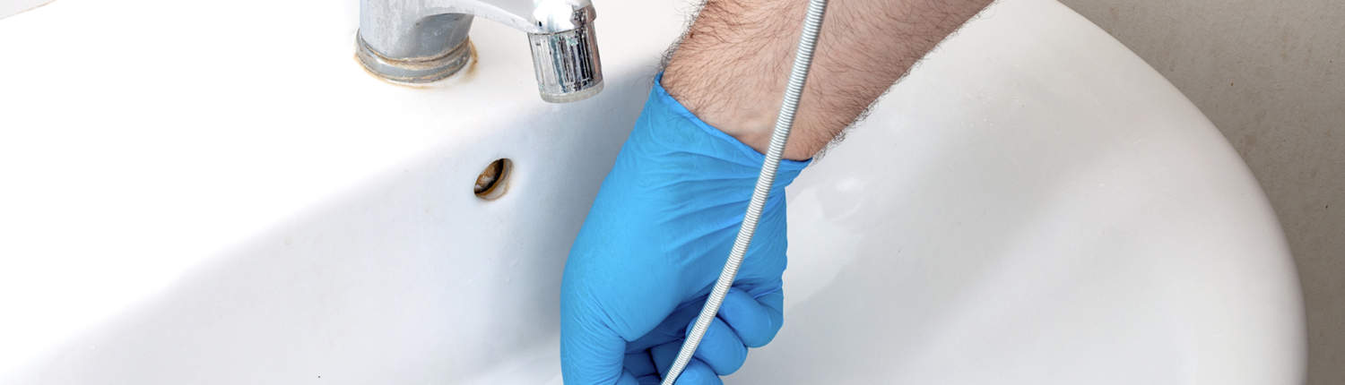 Gloved man cleaning the drain pipe of a bathroom sink