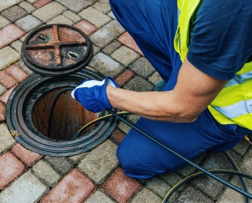 Image of a worker cleaning a blocked sewer line.