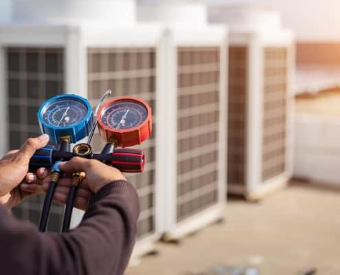 Side view of someone holding a manifold gauge with HVAC units in the background