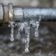 Frozen icicles hanging on gray metal pipe after winter thaw